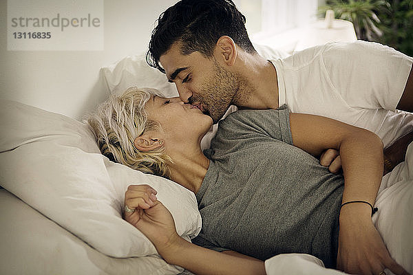 Junges Paar küsst sich zu Hause auf dem Bett