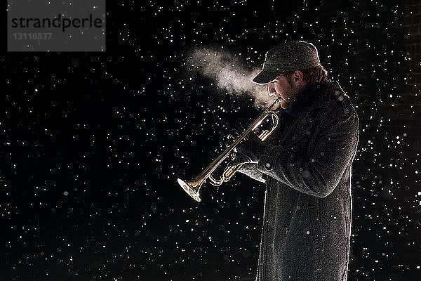 Seitenansicht eines Mannes  der bei Schneefall Trompete spielt