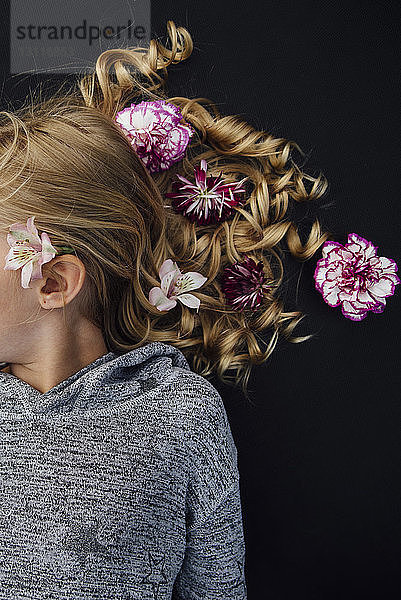 Draufsicht auf ein Mädchen mit Blumen im Haar  das auf schwarzem Hintergrund liegt