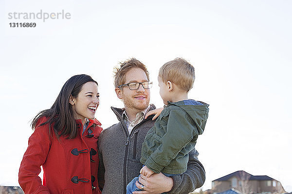 Glückliche Familie in warmer Kleidung vor klarem Himmel stehend