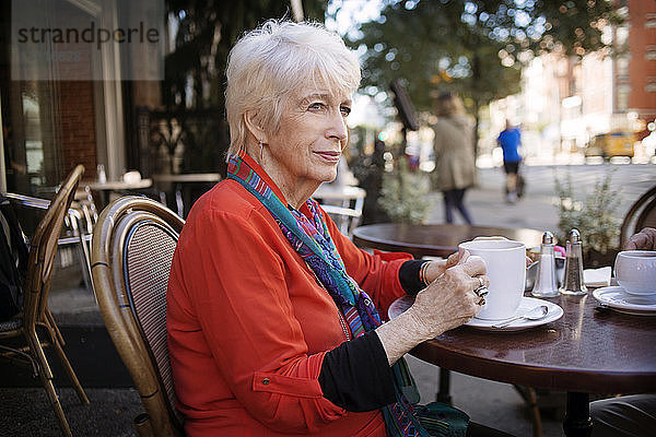 Nachdenkliche ältere Frau hält Kaffeetasse  während sie im Straßencafé sitzt