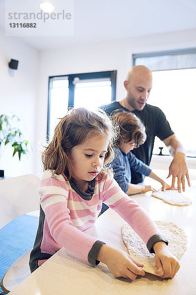 Vater hilft Kindern bei der Zubereitung von Teig bei Tisch zu Hause