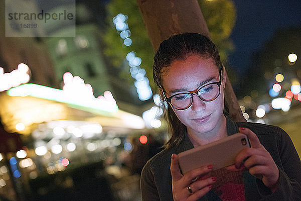 Junge Frau benutzt Smartphone in beleuchteter Stadt bei Nacht