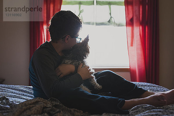 Junge umarmt Hund  während er zu Hause auf dem Bett sitzt