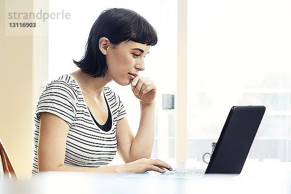 Seitenansicht einer lächelnden Frau  die einen Laptop benutzt  während sie zu Hause sitzt