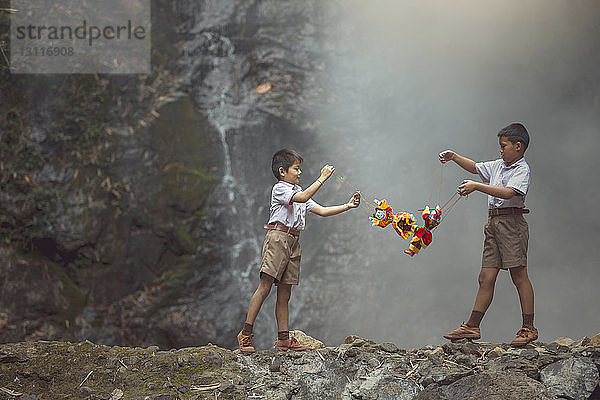 Freunde spielen mit Puppen  während sie auf einer Felsformation vor einem Wasserfall stehen