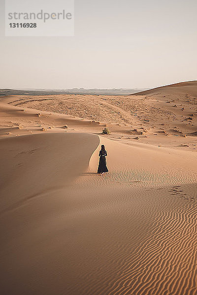 Rückansicht einer Frau  die bei Sonnenuntergang in der Wüste Sahara bei klarem Himmel spazieren geht