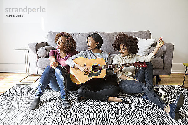 Fröhliche Frau spielt Gitarre für Freundinnen zu Hause