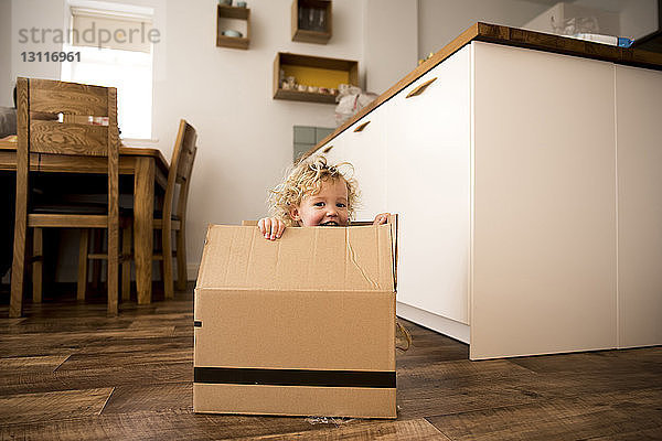 Porträt eines glücklichen Mädchens  das zu Hause in einem Pappkarton sitzt