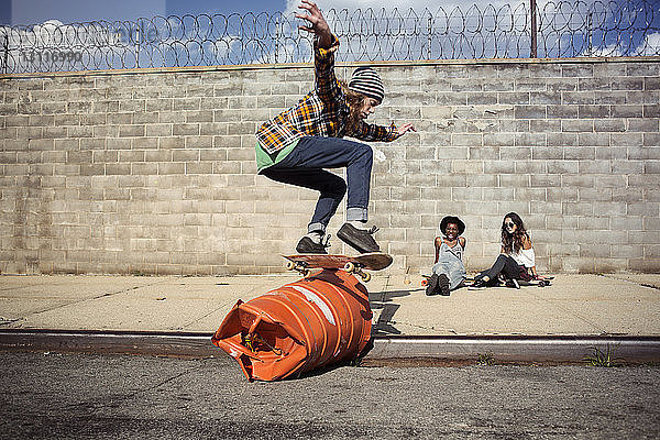 Junger Mann führt Skateboard-Stunt über Fass auf der Straße aus