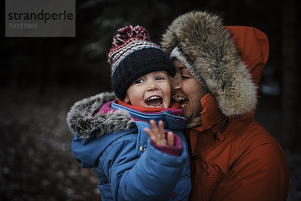 Glückliche Mutter trägt ihre Tochter  während sie im Winter im Wald steht