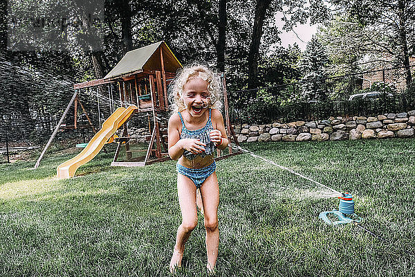 Glückliches Mädchen spielt im Sprinkler im Park