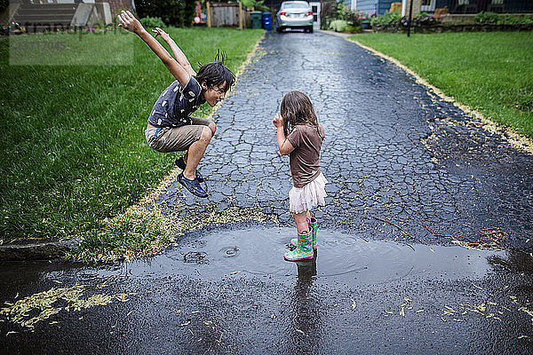 Seitenansicht von verspielten Geschwistern  die sich während der Regenzeit auf nasser Straße vergnügen