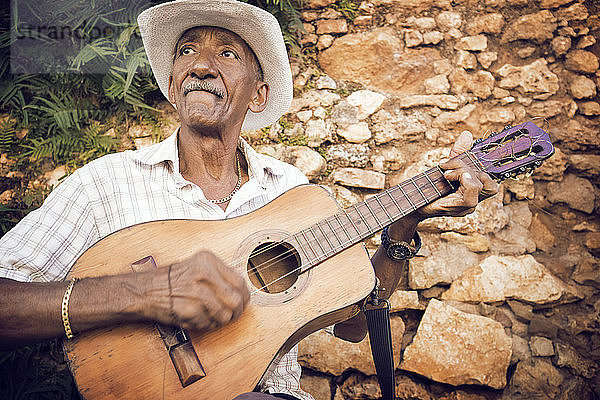 Mann spielt Gitarre  während er an einer Steinmauer sitzt