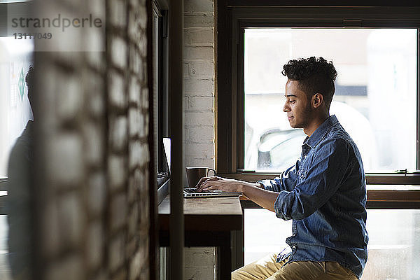 Seitenansicht eines Mannes  der einen Laptop benutzt  während er an den Fenstern eines Cafés sitzt