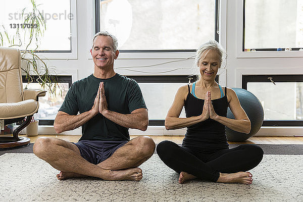Paar in voller Länge mit gefalteten Händen meditiert  während es zu Hause Sport treibt