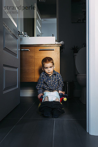 Porträt eines Jungen  der beim Stuhlgang auf dem Töpfchen sitzt  zu Hause durch die Tür gesehen