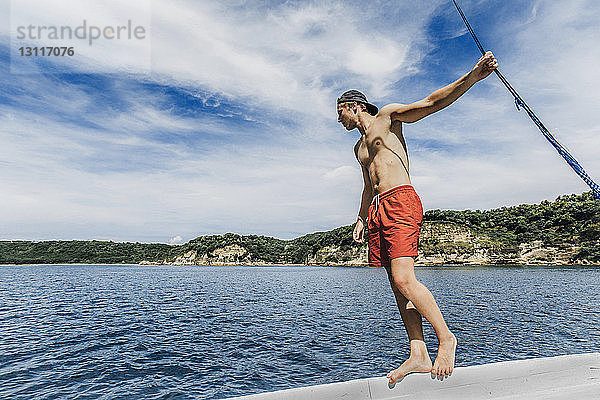 Mann ohne Hemd schaut aufs Meer  während er am sonnigen Tag im Boot vor bewölktem Himmel steht