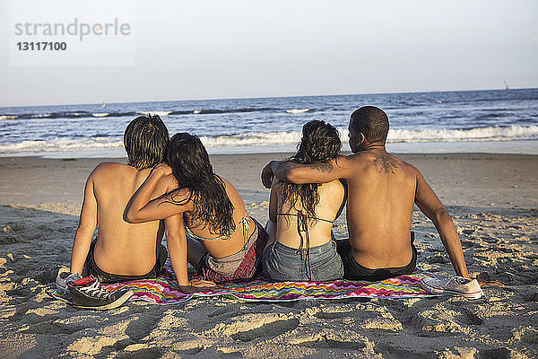 Rückansicht von Paaren  die an einem sonnigen Tag am Strand sitzen