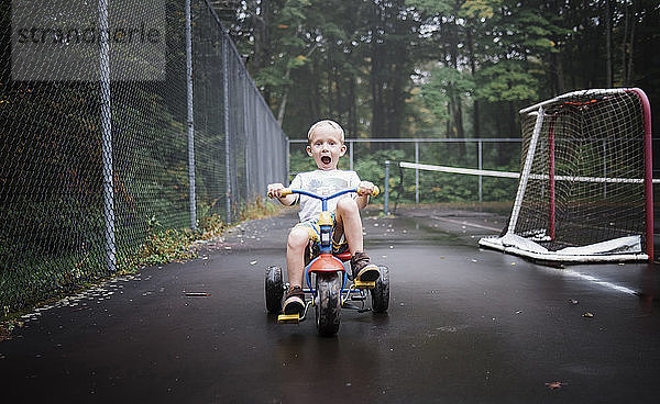 Porträt eines verspielten Jungen auf einem Dreirad auf einem Spielplatz