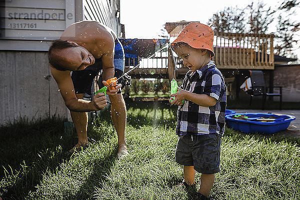Spielerischer Vater  der beim Spielen im Hinterhof mit Spritzpistolen Wasser auf den Sohn spritzt