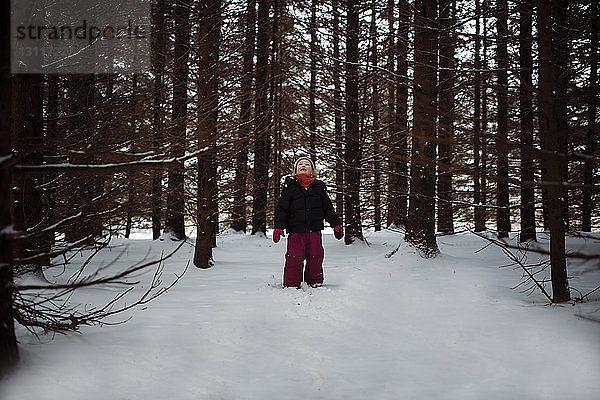 Mädchen schaut auf  während sie auf einem schneebedeckten Feld im Wald steht