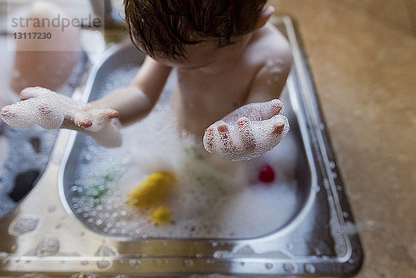 Schrägansicht eines Jungen  der mit Seifenlauge im Waschbecken spielt