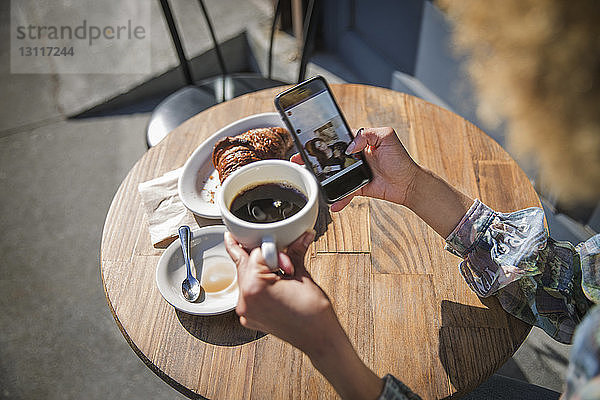 Ausschnitt einer Frau mit Smartphone und Kaffeetasse im Straßencafé