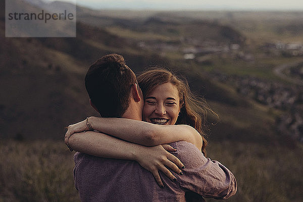 Liebevolles junges Paar umarmt sich auf Feld gegen Berge