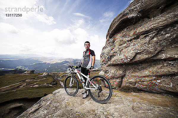 Portrait eines Radfahrers - mit Fahrrad auf Berg gegen Himmel stehend