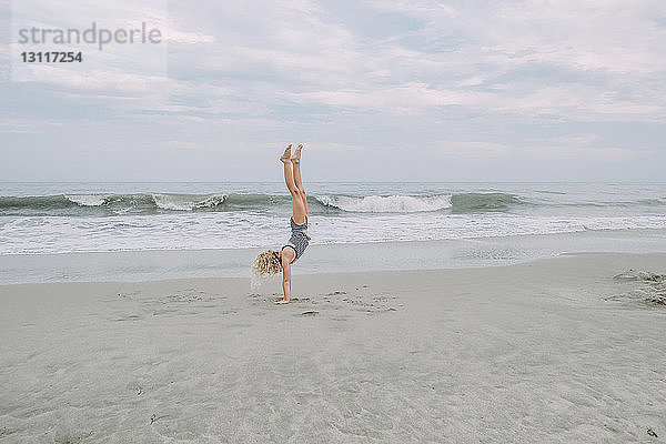 Mädchen in voller Länge beim Handstand am Cape May Beach gegen Meer und Himmel