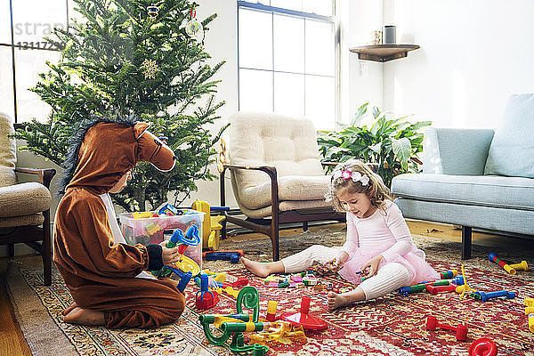 Geschwister spielen mit Bauklötzen  während sie zu Hause am Weihnachtsbaum sitzen