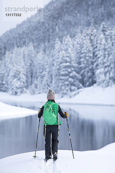 Rückansicht einer Wanderin  die am schneebedeckten Seeufer steht