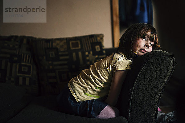 Gelangweiltes Mädchen schaut weg  während es auf dem Sofa kniet