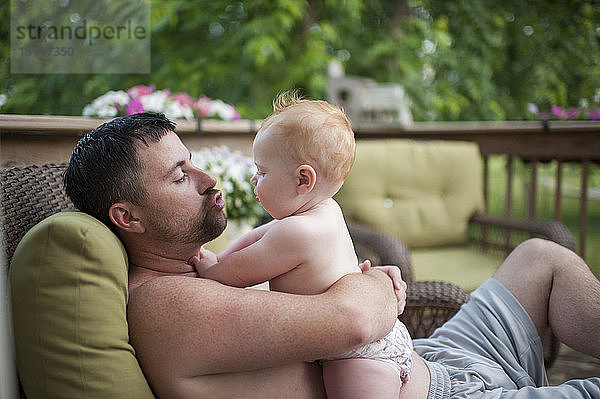 Vater ohne Hemd spielt mit Sohn  während er sich auf der Veranda entspannt