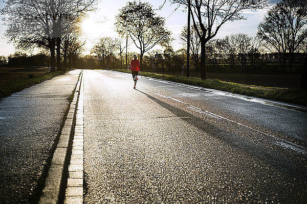 Mittelstrecke einer Frau  die bei Sonnenuntergang auf der Straße läuft