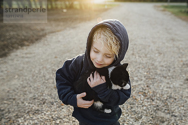 Hochwinkelansicht eines süßen Jungen  der eine Katze im Park umarmt