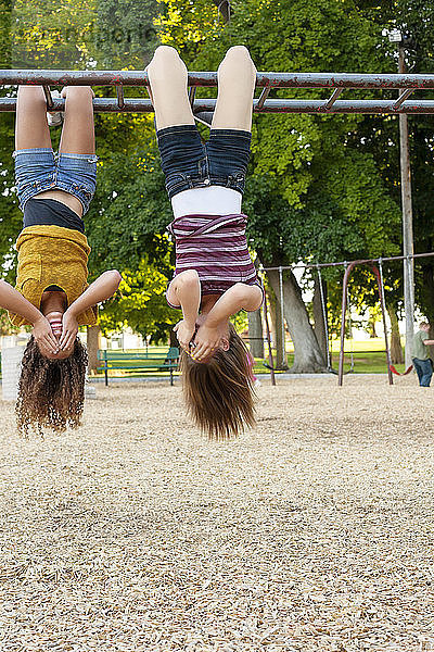 Freunde bedecken ihr Gesicht  während sie kopfüber im Klettergerüst auf dem Spielplatz hängen