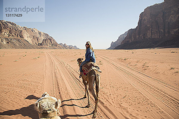 Weibliche Touristin schaut beim Kamelreiten in der Wüste über die Schulter