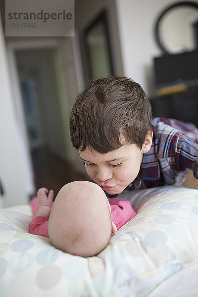 Bruder küsst kleines Mädchen  das zu Hause auf dem Bett liegt