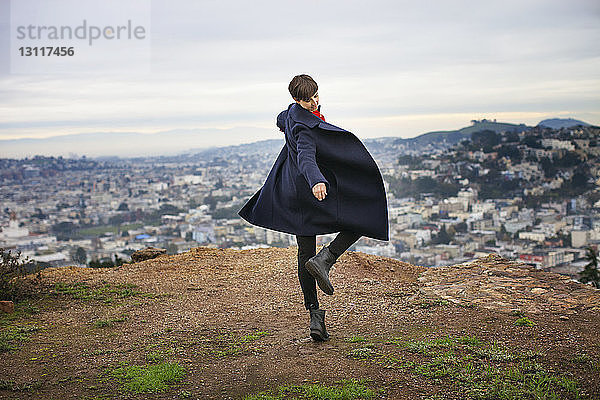 Unbekümmerte Frau tanzt auf dem Berggipfel mit der Stadtlandschaft im Hintergrund