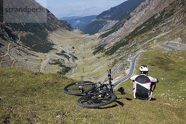 Rückansicht eines männlichen Athleten  der mit dem Fahrrad auf einem Berg sitzt