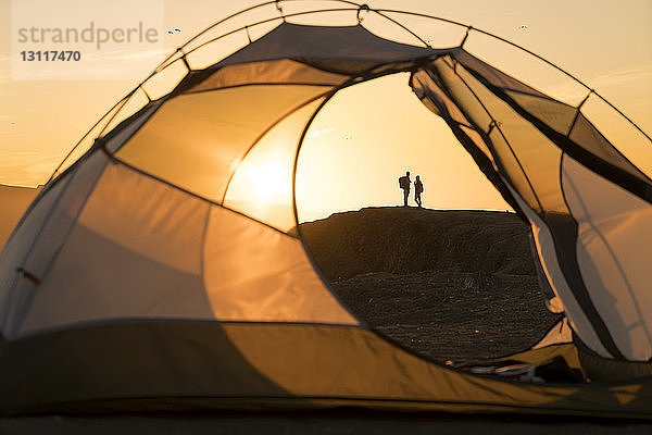 Fernsicht auf ein Paar  das auf einer Felsformation steht  durch ein Zelt bei Sonnenuntergang gesehen