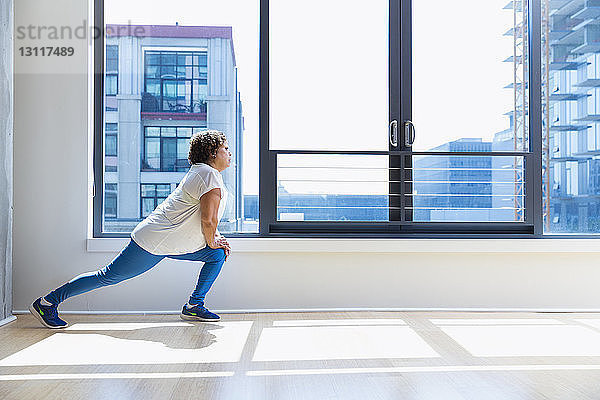 Frau in voller Länge  die im Yoga-Studio die Beine gegen das Fenster streckt