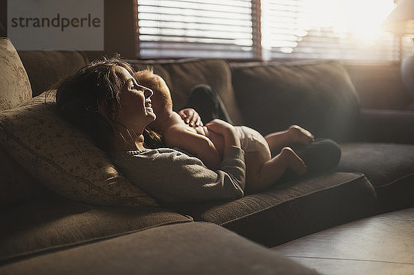 Lächelndes Mädchen umarmt den Bruder  während es zu Hause auf dem Sofa liegt