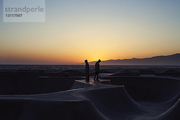 Silhouetten-Skateboarder stehen bei Sonnenuntergang auf der Rampe vor klarem Himmel
