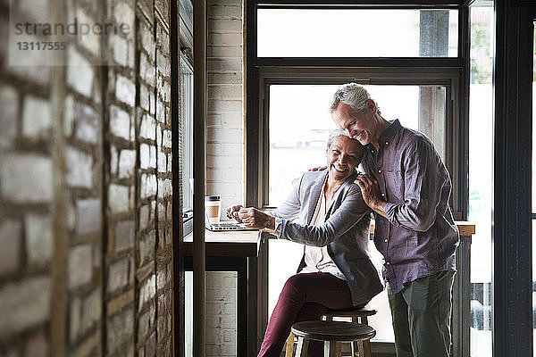 Lächelndes Paar umarmt sich an den Fenstern eines Cafés