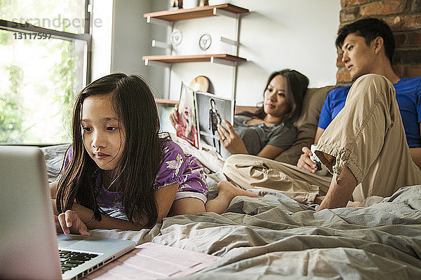 Mädchen benutzt Laptop-Computer  während sie zu Hause mit den Eltern im Bett sitzt