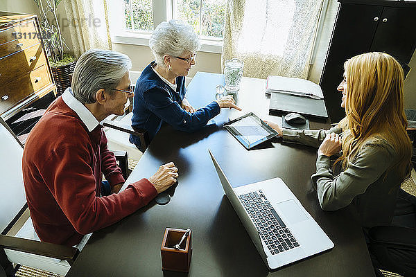 Schrägansicht des Finanzberaters  der dem älteren Ehepaar den Plan auf einem Tablet-Computer im Büro erklärt