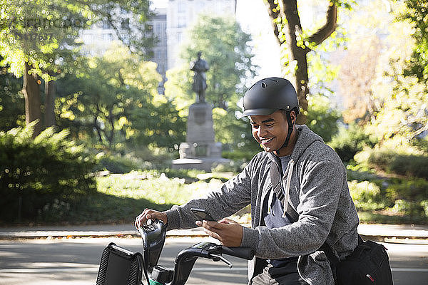 Lächelnder Mann benutzt Mobiltelefon beim Fahrradfahren auf Stadtstraße
